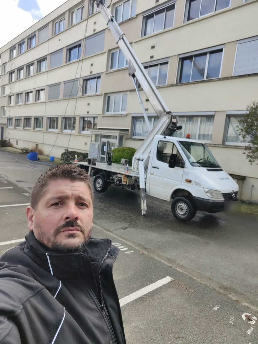 Antoine Faucheux devant un camion à nacelle, au pied d'un immeuble dont la façade est en cours de nettoyage