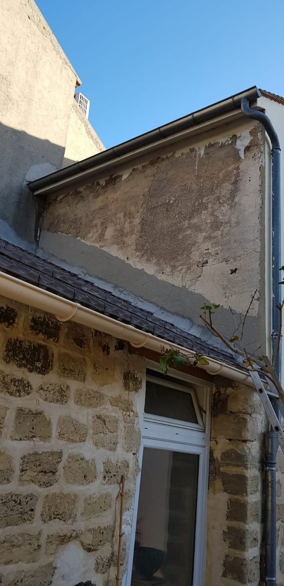 Pignon d'une maison dont l'ancien enduit a été retiré, support à nu au-dessus d'un mur en moellons de pierre