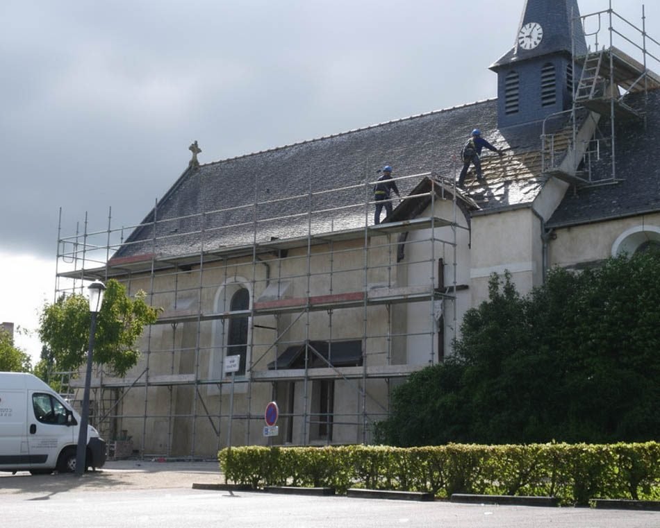 Couvreurs au travail sur la toiture en ardoise d'une église, échafaudage monté sur toute la longueur de la façade