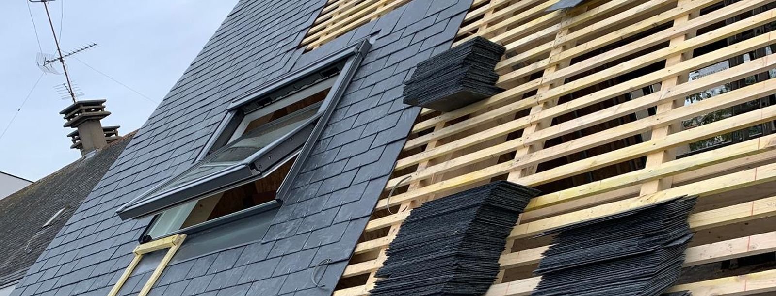 Fenêtre de toit posée dans une couverture en ardoise neuve, ardoises empilées à côté