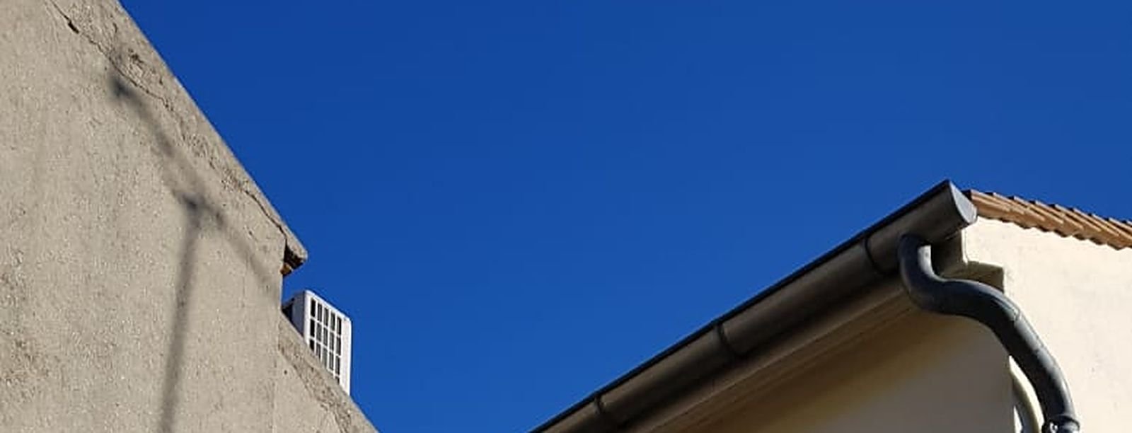 Pignon enduit sous un ciel bleu, gouttière et rive de toiture en bas de l'image